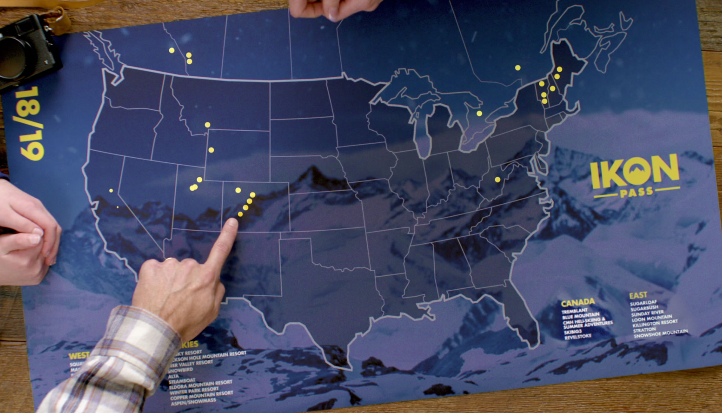 Ikon Pass map on coffee table with finger pointing at a ski resort